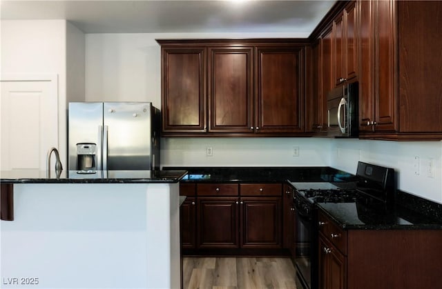 kitchen featuring dark stone counters, dark brown cabinets, stainless steel appliances, sink, and light hardwood / wood-style flooring