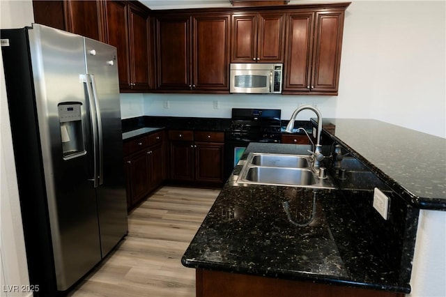 kitchen featuring dark brown cabinetry, sink, dark stone countertops, light hardwood / wood-style floors, and appliances with stainless steel finishes