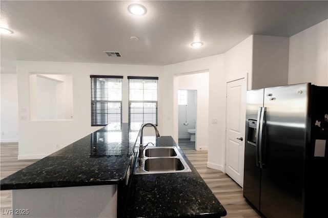 kitchen with dark stone countertops, sink, an island with sink, and stainless steel refrigerator with ice dispenser