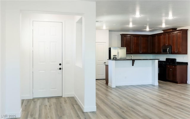 kitchen featuring a kitchen breakfast bar, dark brown cabinetry, light hardwood / wood-style flooring, and appliances with stainless steel finishes