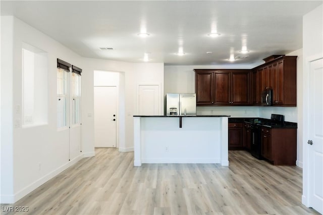 kitchen with a breakfast bar, a kitchen island with sink, light wood-type flooring, appliances with stainless steel finishes, and dark brown cabinetry