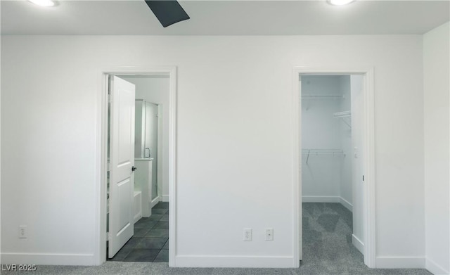 unfurnished bedroom with connected bathroom, ceiling fan, a walk in closet, a closet, and dark carpet