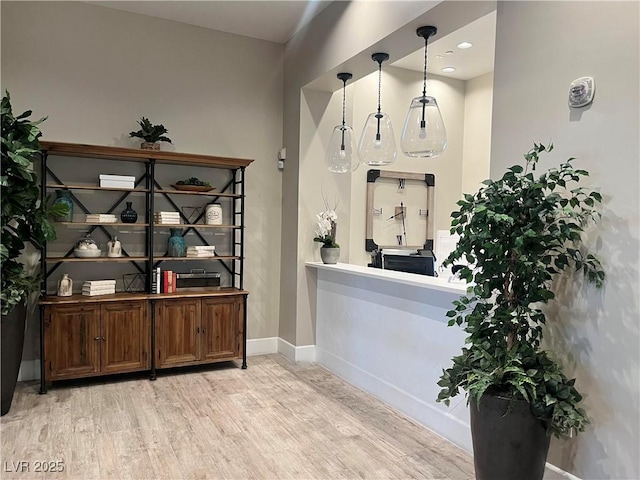 bar featuring dark brown cabinets, light hardwood / wood-style flooring, and hanging light fixtures