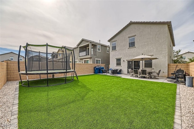 rear view of property featuring a yard, a trampoline, and a patio area