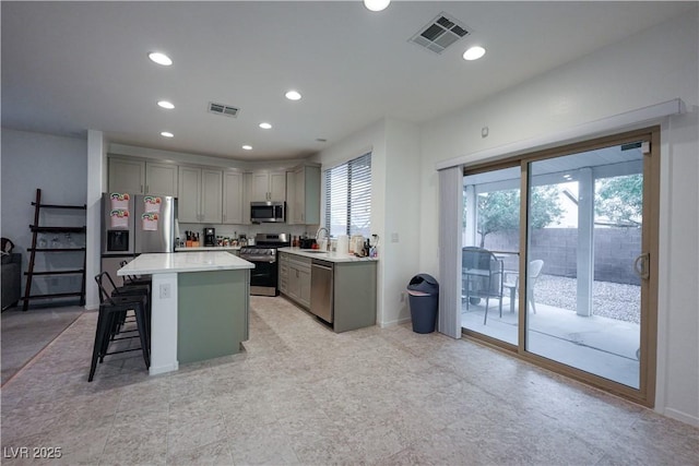 kitchen with a kitchen bar, gray cabinetry, stainless steel appliances, sink, and a center island