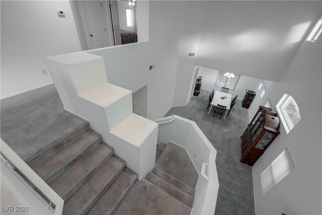 stairway featuring carpet, a high ceiling, and a notable chandelier