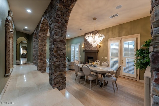 dining space featuring light wood-type flooring, ornate columns, a fireplace, and a chandelier