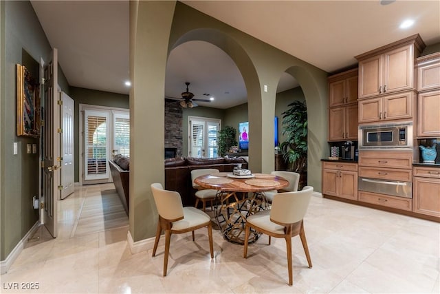 dining area with light tile patterned floors, a stone fireplace, and ceiling fan