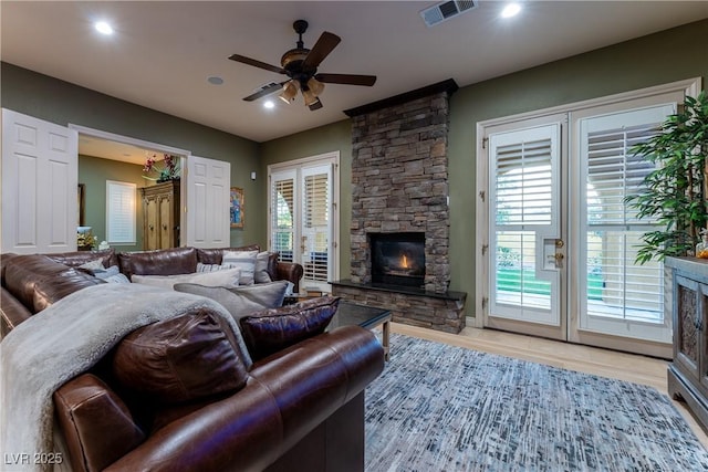 living room with light hardwood / wood-style floors, a stone fireplace, ceiling fan, and plenty of natural light