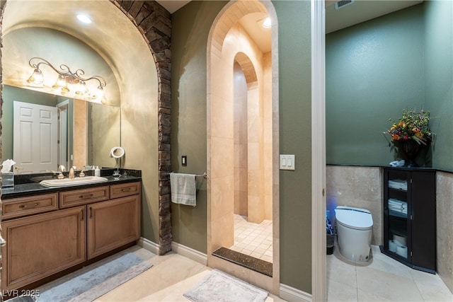 bathroom with tile patterned flooring, vanity, toilet, and a tile shower