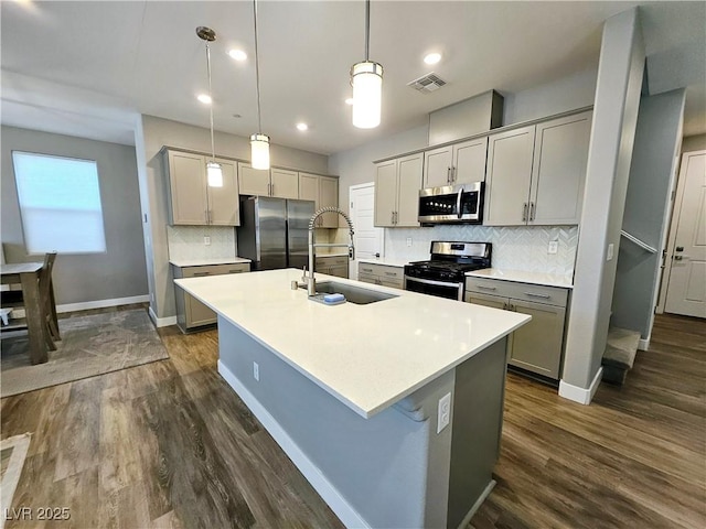 kitchen with sink, dark hardwood / wood-style floors, an island with sink, appliances with stainless steel finishes, and decorative light fixtures