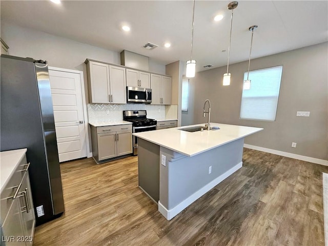 kitchen with appliances with stainless steel finishes, sink, decorative light fixtures, a center island with sink, and gray cabinets