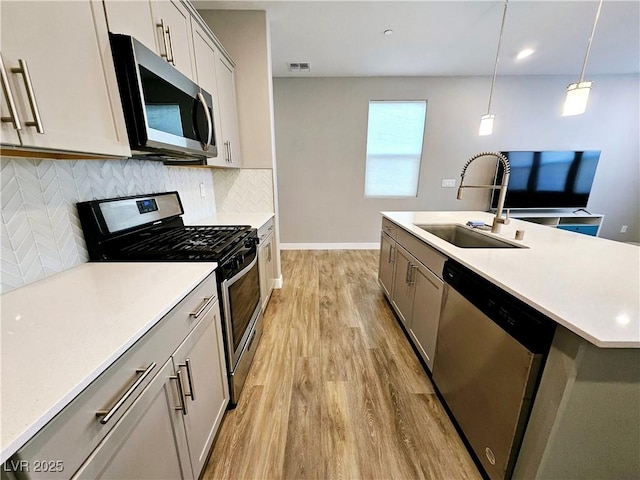 kitchen featuring stainless steel appliances, a kitchen island with sink, sink, pendant lighting, and light hardwood / wood-style floors