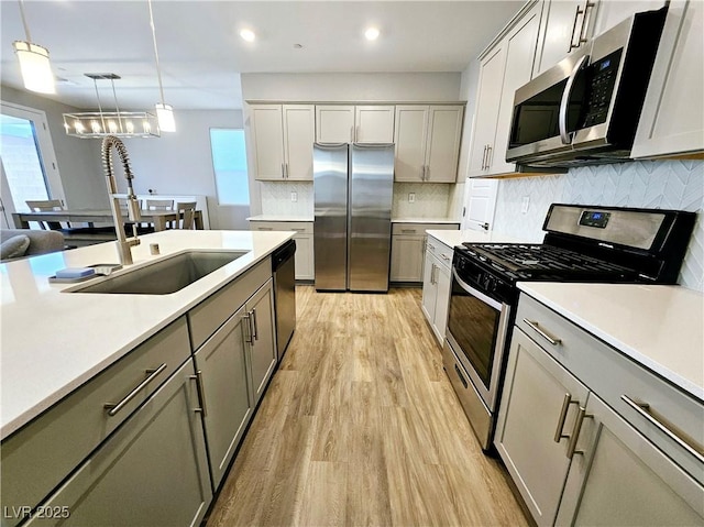 kitchen featuring gray cabinetry, sink, appliances with stainless steel finishes, decorative light fixtures, and light hardwood / wood-style floors