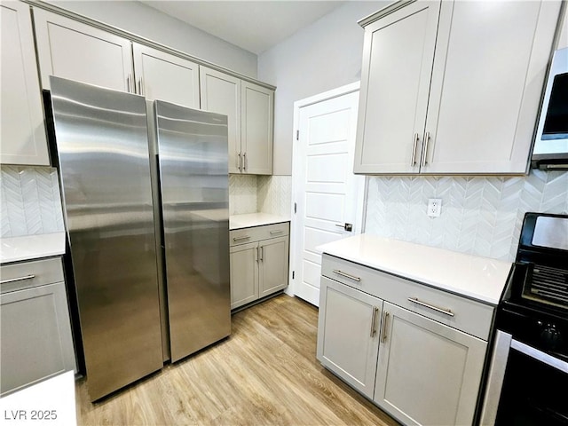 kitchen with decorative backsplash, electric range oven, gray cabinetry, light hardwood / wood-style flooring, and stainless steel refrigerator