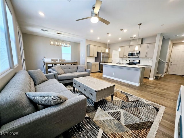 living room with sink, ceiling fan with notable chandelier, and light wood-type flooring