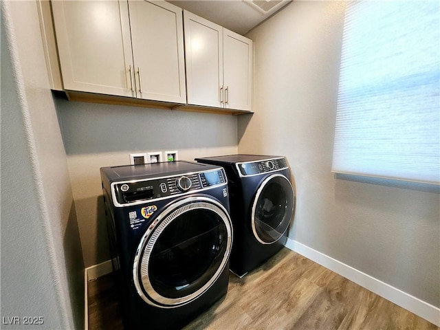 washroom with washing machine and clothes dryer, cabinets, and light wood-type flooring