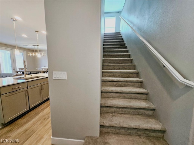 stairway with a notable chandelier, a healthy amount of sunlight, wood-type flooring, and sink