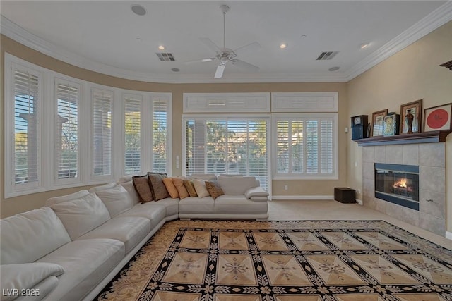 carpeted living room with a tiled fireplace, ceiling fan, crown molding, and plenty of natural light