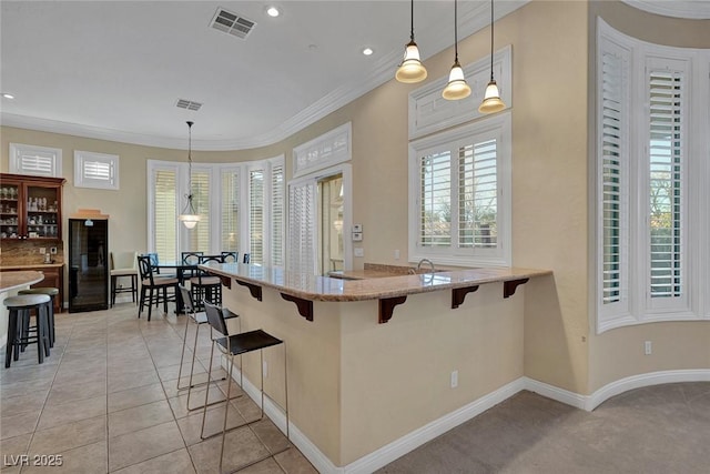 kitchen with kitchen peninsula, light stone counters, ornamental molding, decorative light fixtures, and a breakfast bar area