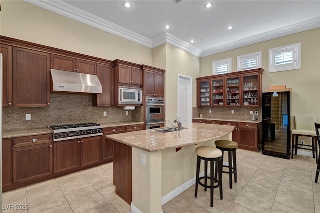 kitchen featuring light stone counters, an island with sink, stainless steel appliances, and ornamental molding