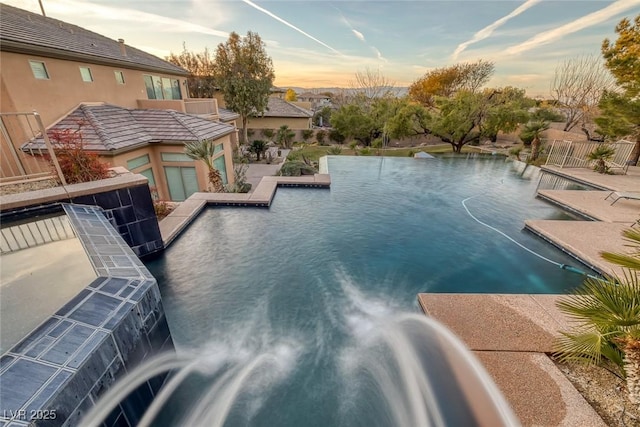 pool at dusk featuring a patio area and pool water feature