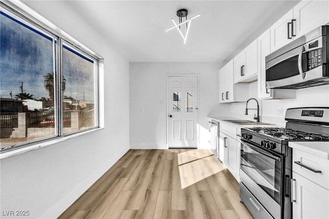 kitchen with appliances with stainless steel finishes, light wood-type flooring, white cabinetry, and sink