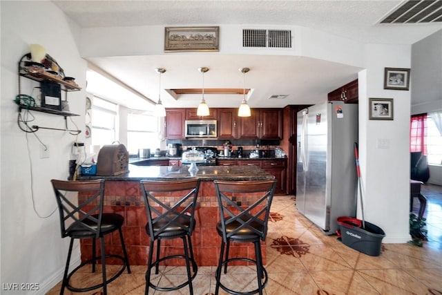 kitchen with hanging light fixtures, stainless steel appliances, a kitchen breakfast bar, kitchen peninsula, and light tile patterned flooring