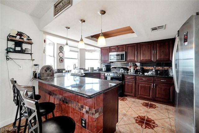 kitchen with a kitchen bar, kitchen peninsula, dark stone counters, stainless steel appliances, and a tray ceiling