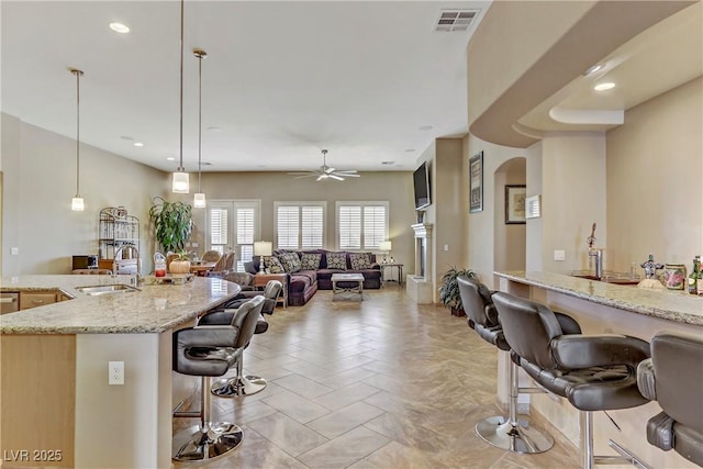 kitchen with light stone countertops, ceiling fan, sink, pendant lighting, and a breakfast bar