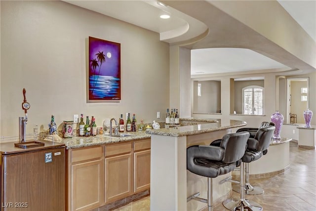 bar featuring light brown cabinetry, light stone countertops, and sink