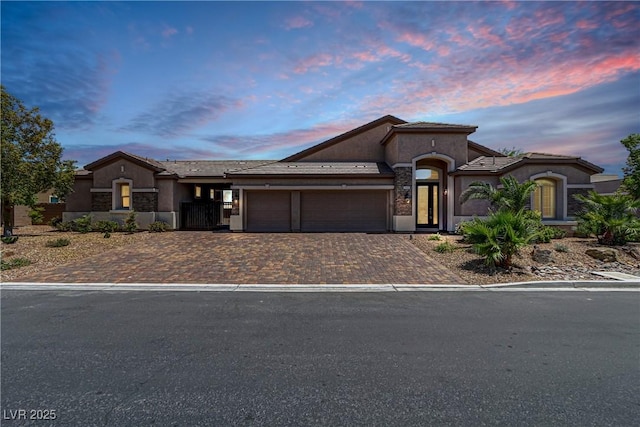 view of front of house with an attached garage, stone siding, decorative driveway, and stucco siding