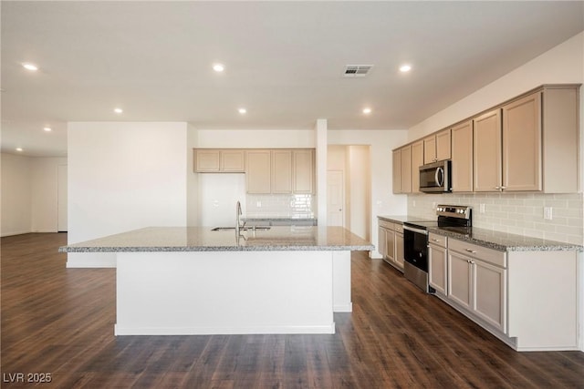 kitchen with sink, dark wood-type flooring, stainless steel appliances, light stone counters, and a center island with sink