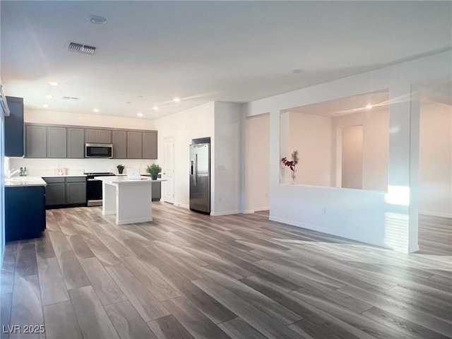 kitchen with gray cabinets, a kitchen island, stainless steel appliances, and light wood-type flooring