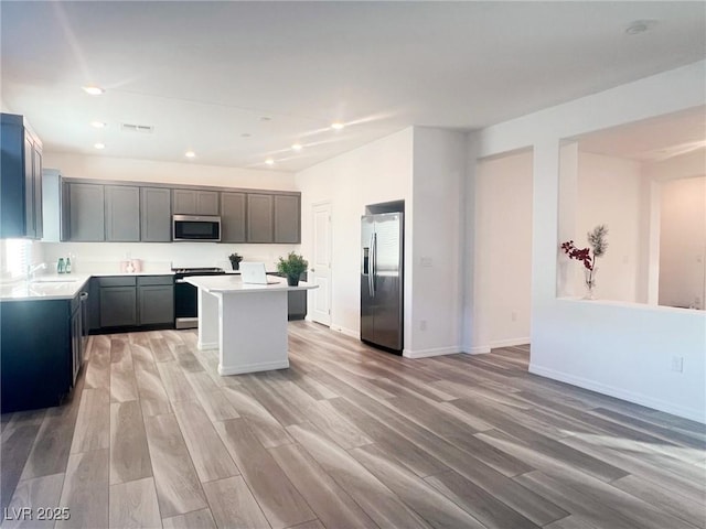 kitchen featuring light wood-type flooring, appliances with stainless steel finishes, a center island, and sink