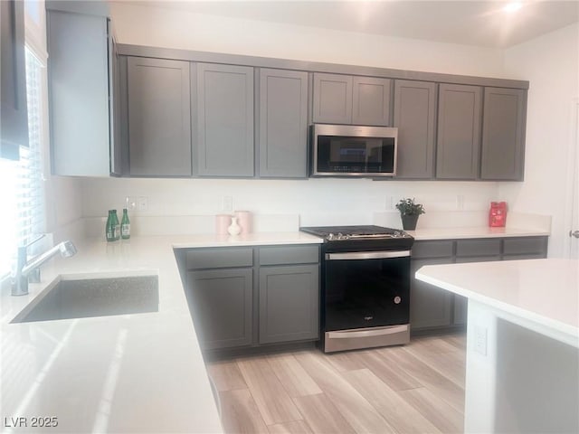 kitchen featuring gray cabinets, light wood-type flooring, sink, and appliances with stainless steel finishes