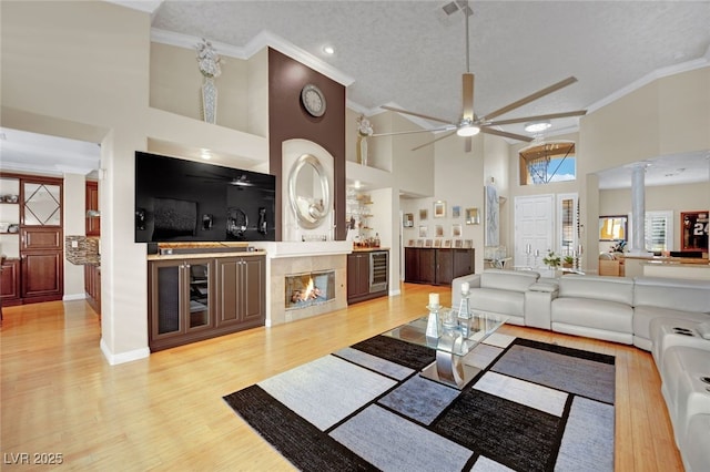 living room featuring a high ceiling, crown molding, a textured ceiling, and light hardwood / wood-style floors