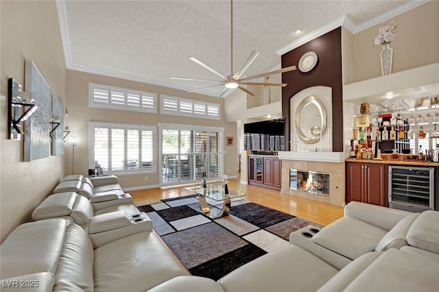 living room featuring crown molding, a tile fireplace, ceiling fan, high vaulted ceiling, and beverage cooler