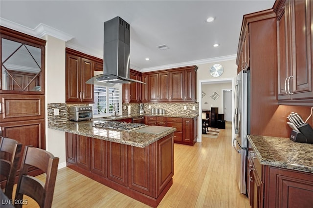 kitchen featuring island exhaust hood, ornamental molding, light stone counters, kitchen peninsula, and stainless steel appliances