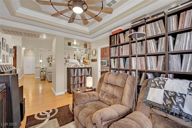 sitting room featuring crown molding, light hardwood / wood-style flooring, a raised ceiling, and ceiling fan