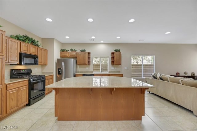 kitchen featuring a center island, sink, light stone counters, a breakfast bar, and black appliances