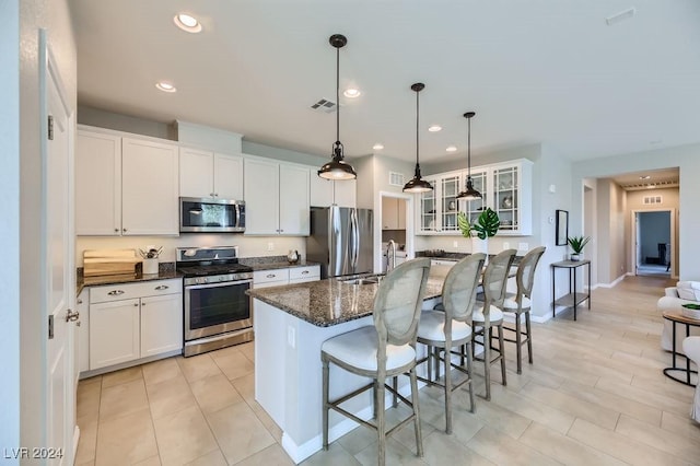 kitchen with white cabinetry, decorative light fixtures, a kitchen island with sink, a breakfast bar, and appliances with stainless steel finishes