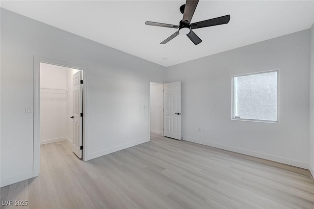 unfurnished bedroom with ceiling fan, a closet, a spacious closet, and light hardwood / wood-style flooring