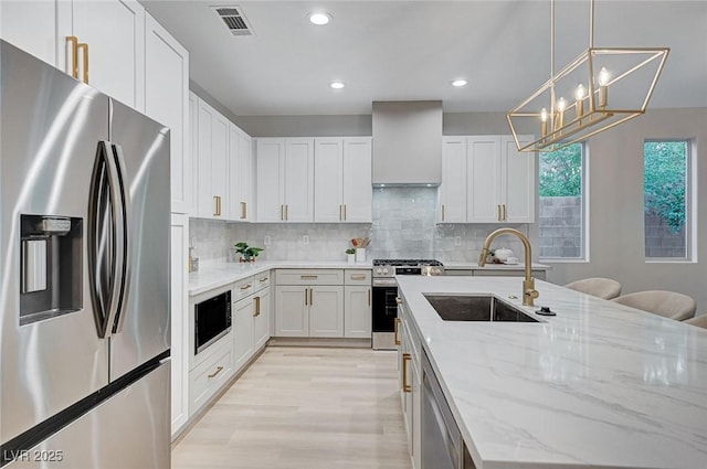 kitchen with white cabinets, sink, wall chimney exhaust hood, light stone countertops, and stainless steel appliances