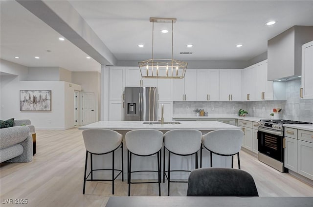 kitchen with sink, hanging light fixtures, a kitchen island with sink, white cabinets, and appliances with stainless steel finishes