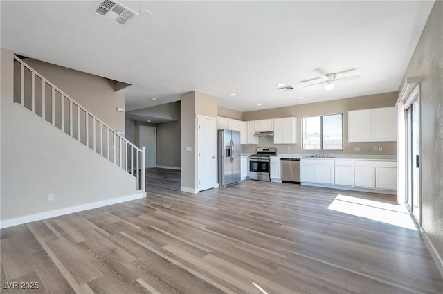 kitchen with stainless steel appliances, ceiling fan, sink, white cabinets, and light hardwood / wood-style floors