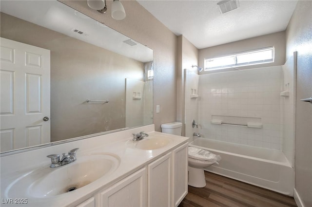 full bathroom featuring vanity, a textured ceiling,  shower combination, hardwood / wood-style flooring, and toilet