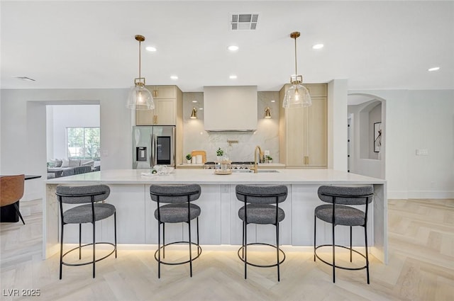 kitchen with stainless steel fridge, hanging light fixtures, a large island with sink, and a breakfast bar area