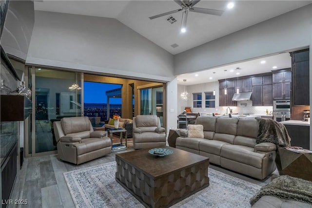 living room with ceiling fan with notable chandelier, light hardwood / wood-style floors, high vaulted ceiling, and sink