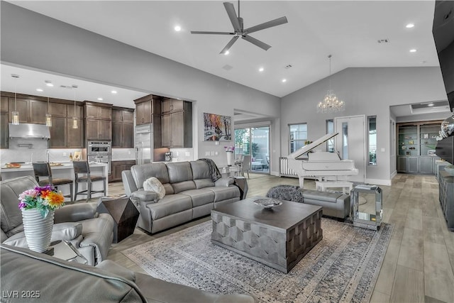 living room with ceiling fan with notable chandelier, light hardwood / wood-style floors, and high vaulted ceiling